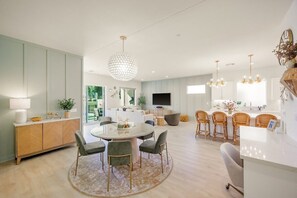 A modern kitchen with a dining area, a large chandelier, and a flat-screen TV. - Fairway Gem: Pool+Spa, Putting Green, EV Charger! (Indio)