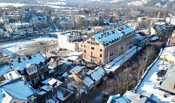 A historic building with a symmetrical facade and a central entrance, surrounded by snow-covered rooftops and adjacent buildings.