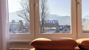 Une pièce avec vue sur un bâtiment et des montagnes, vue à travers une fenêtre.