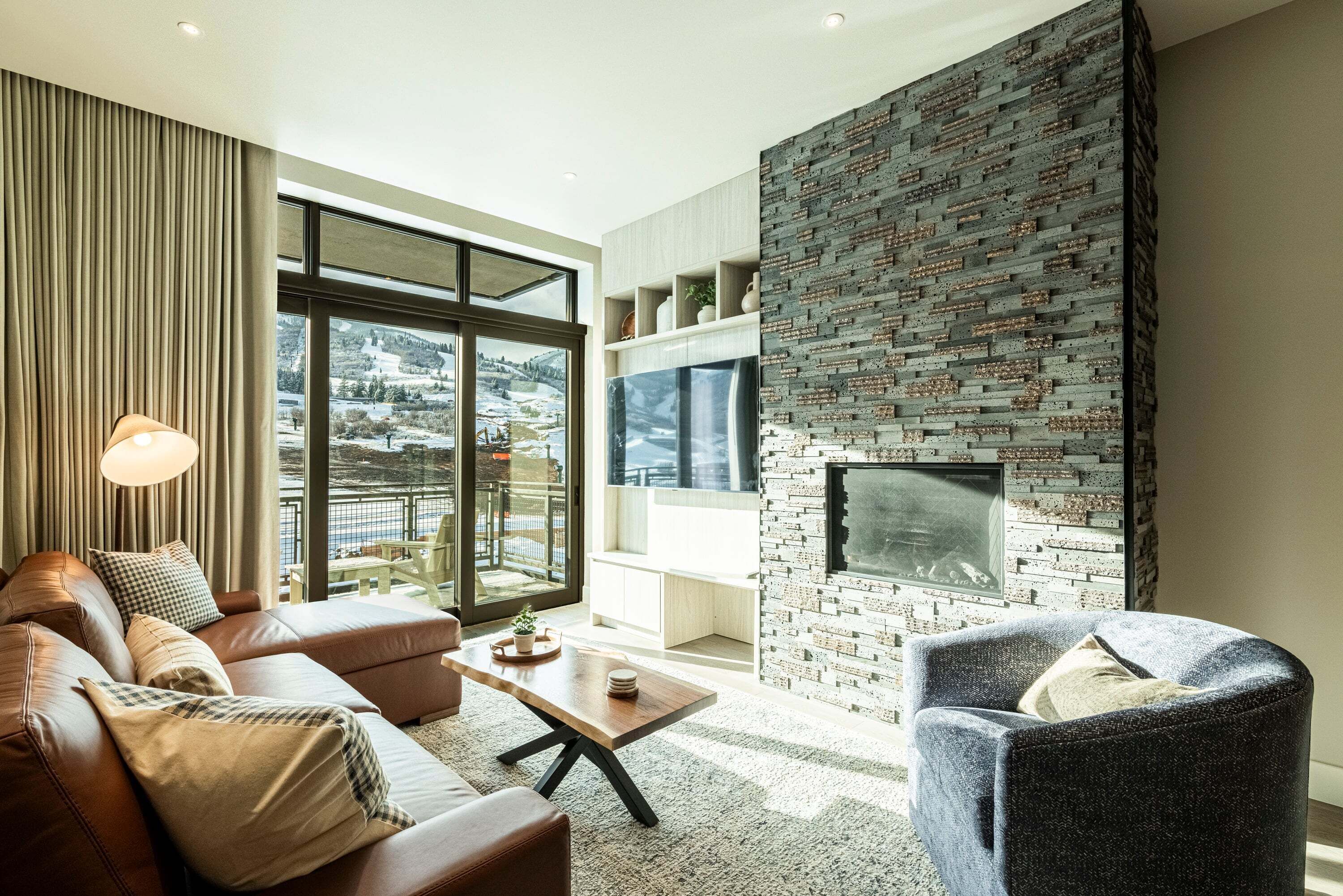 Una sala de estar moderna con un sofá de cuero, una mesa de centro de madera, un sillón azul y una chimenea con pared de ladrillo.