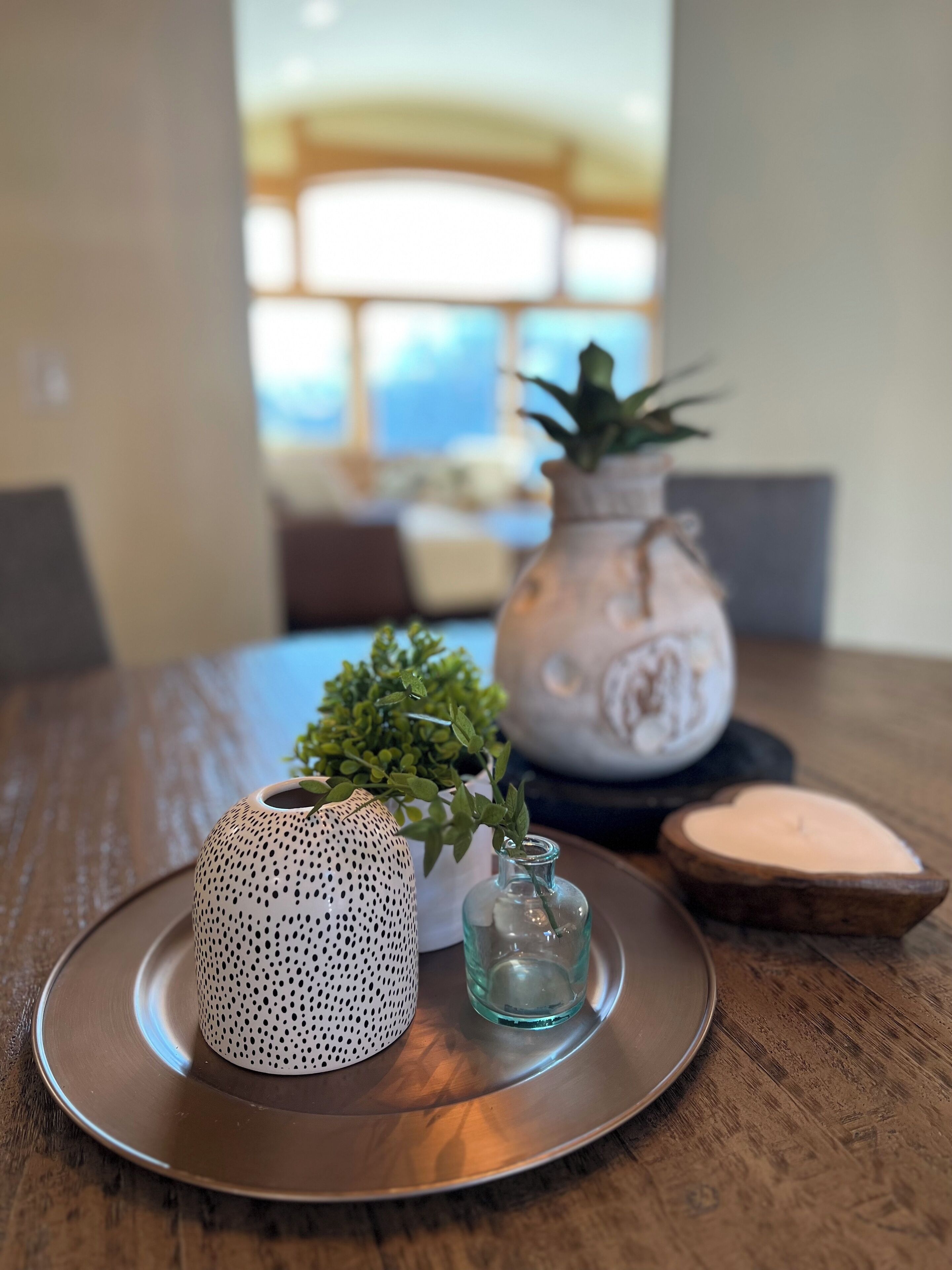 A dining table with a decorative plate, a patterned vase, a small glass vase, and a potted plant.