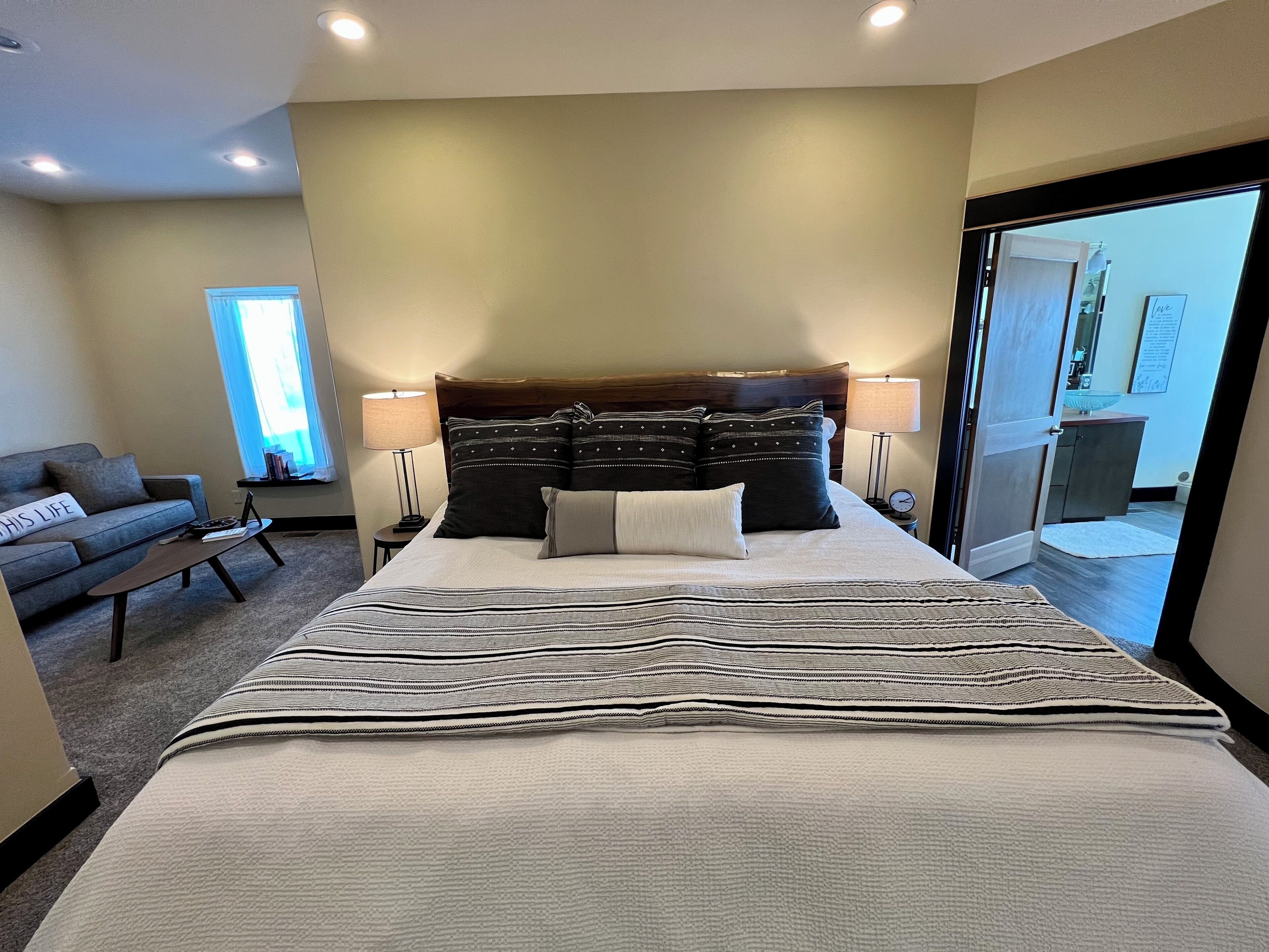 A hotel room with a large bed, two bedside tables with lamps, a sofa, and a view of the outside through a sliding door.