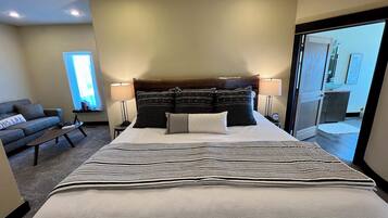 A hotel room with a large bed, two bedside tables with lamps, a sofa, and a view of the outside through a sliding door.