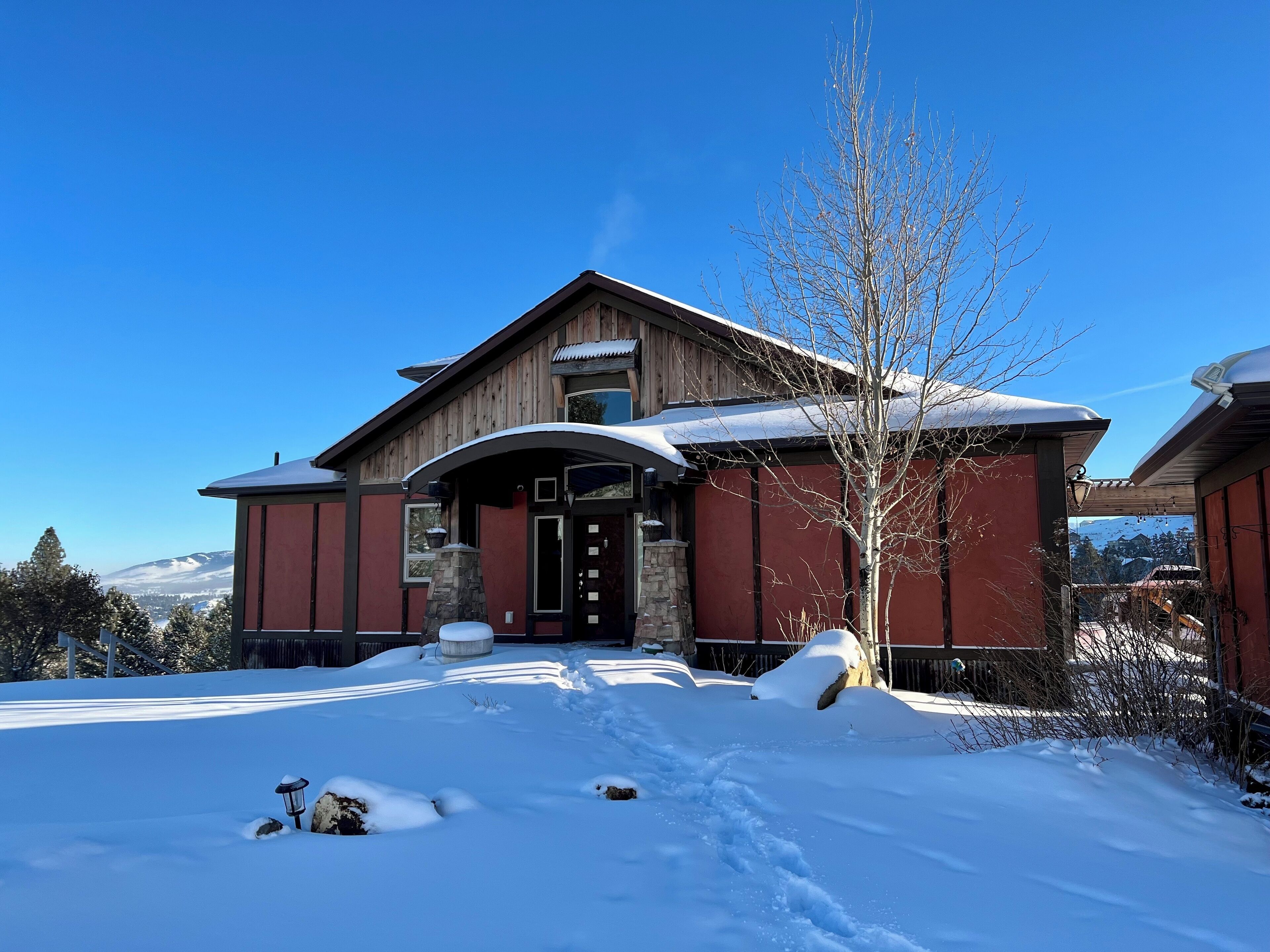 A wooden house with a stone fireplace, a covered entryway, and a snow-covered roof.