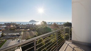 A balcony with a metal railing overlooking a coastal area with buildings, a clear sky, and the sun shining. - Apartment 'Iris' with Sea View, Private Terrace and Air Conditioning (Albenga)