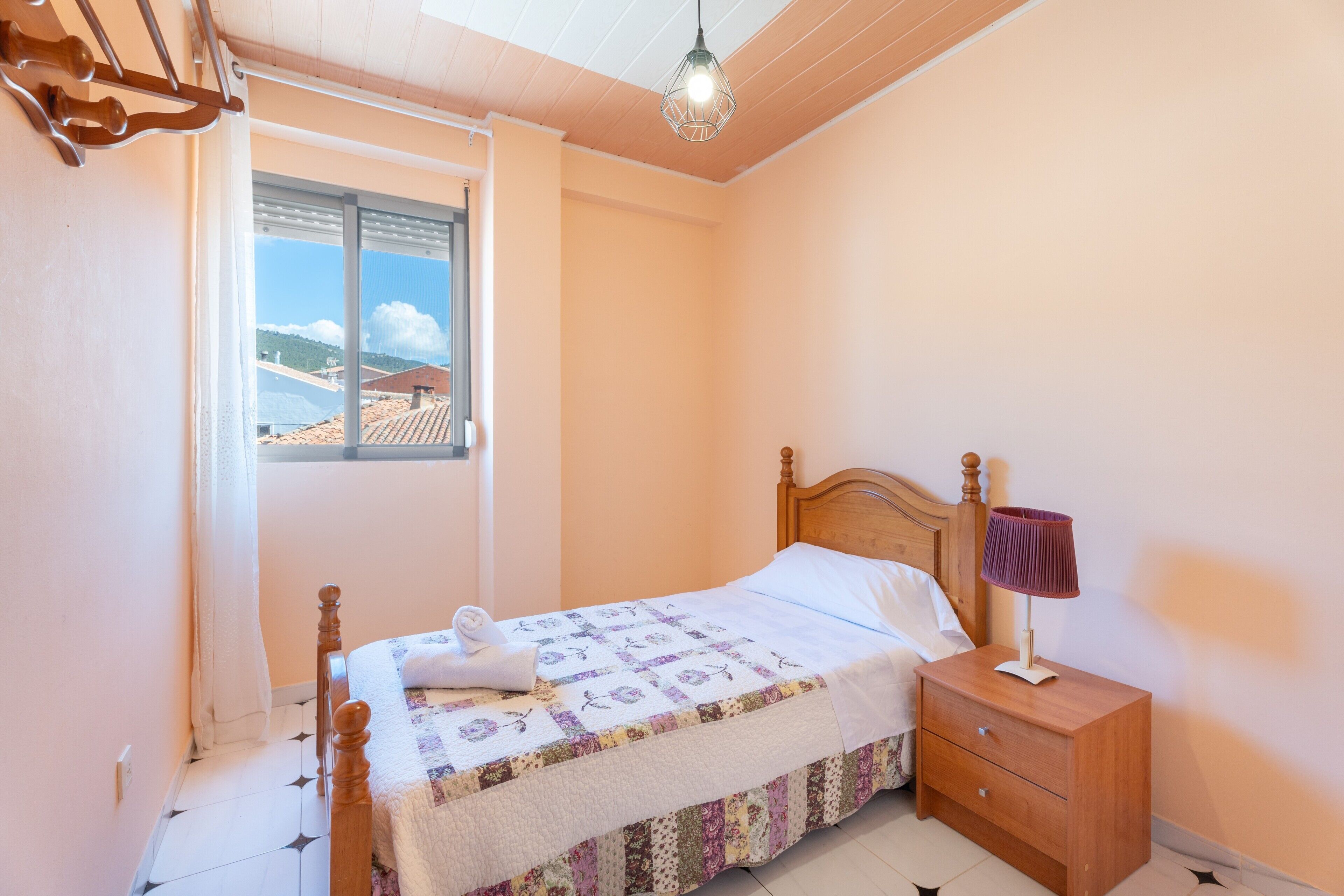 Un dormitorio con cama, mesita de noche, ventana con vistas y lámpara colgante.