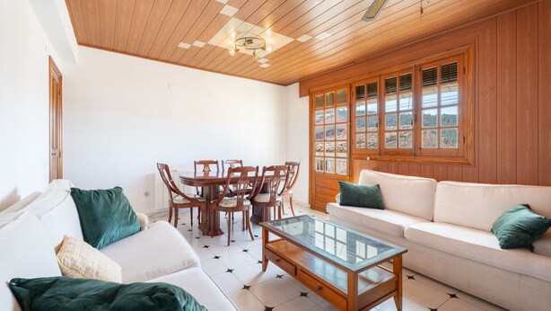 Ein Wohnzimmer mit Holzboden, einem Esstisch mit Stühlen, einer Couch und einem Glastisch.