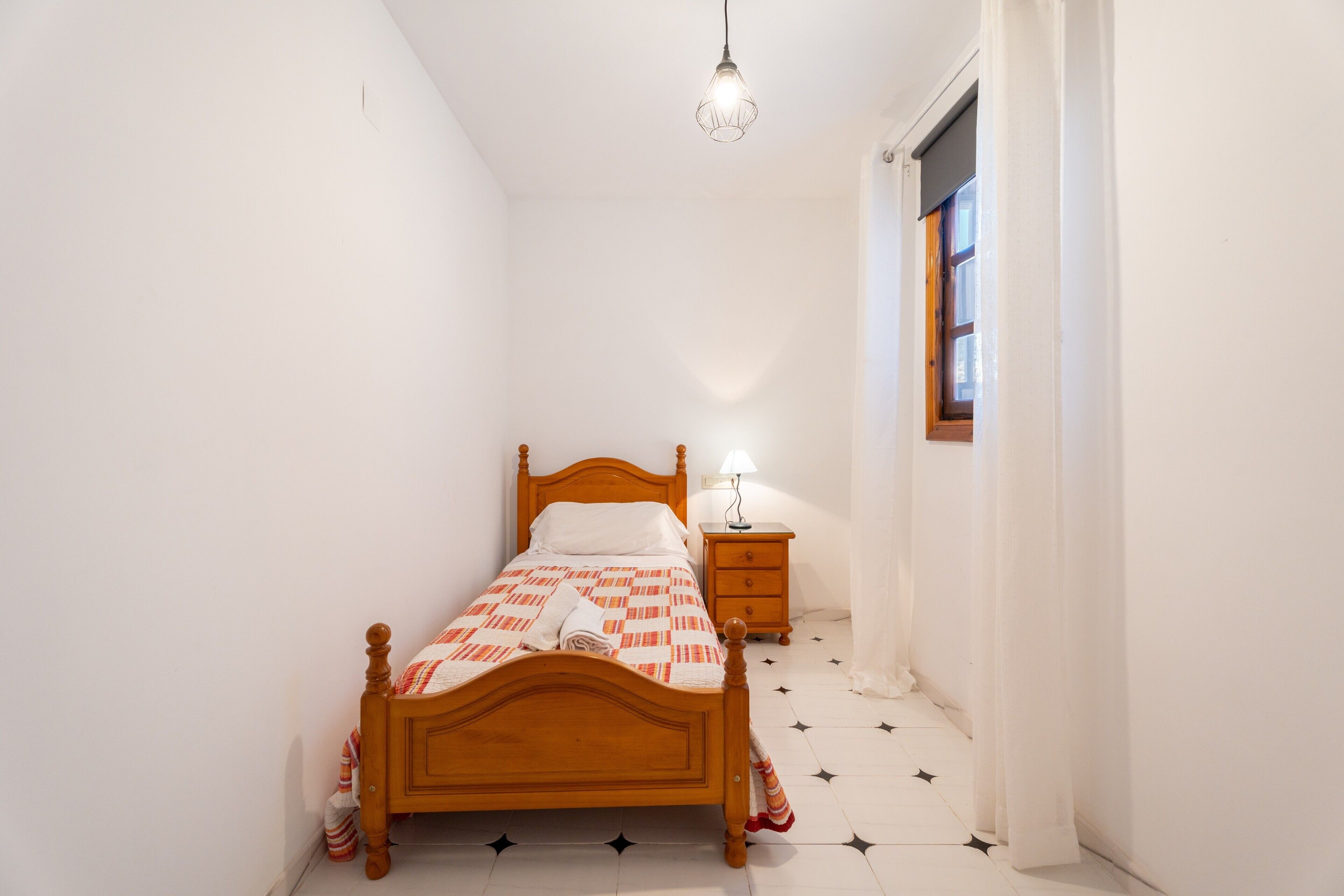 Une chambre à coucher avec un lit en bois, une table de chevet, une lampe et une fenêtre avec des rideaux.
