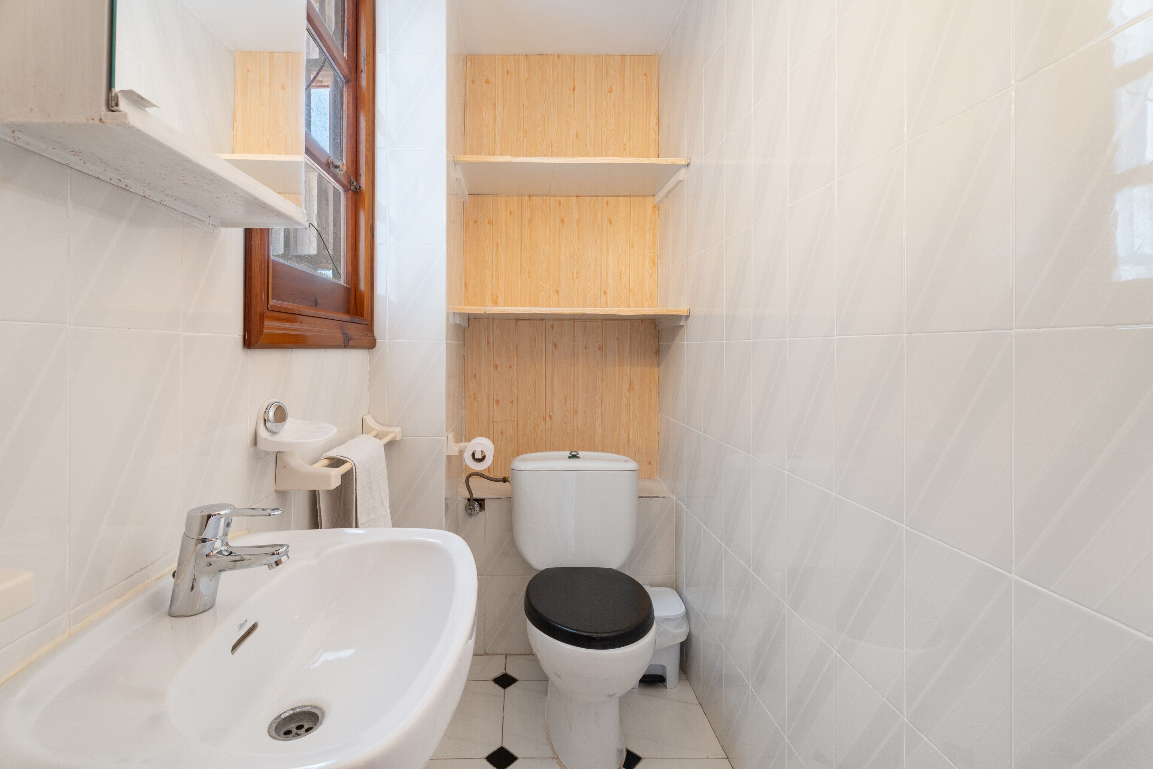 Un baño con un lavabo blanco, un inodoro y estantes de madera.
