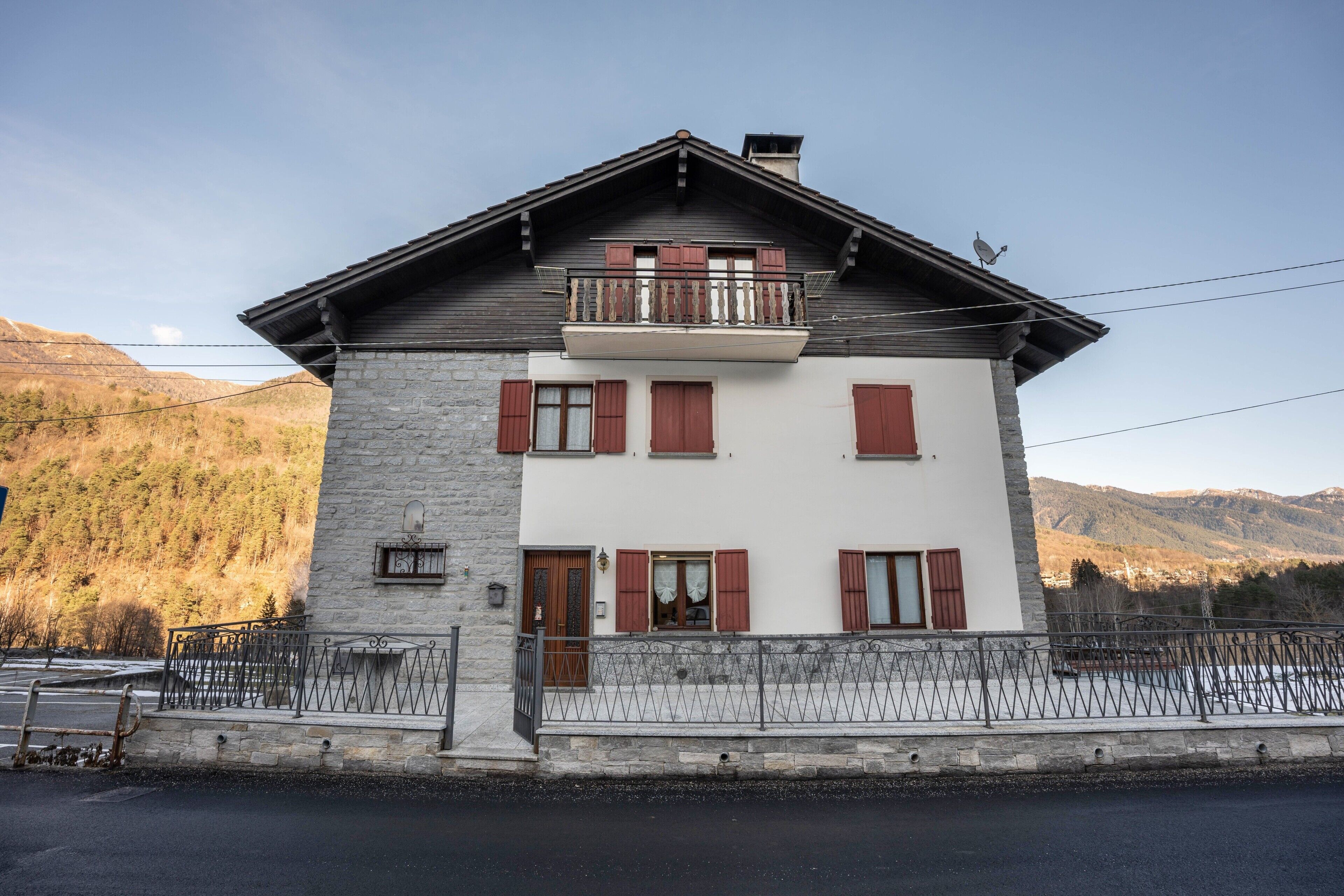 Un bâtiment à deux étages, doté d’une façade en pierre, d’un balcon et surplombant un paysage montagneux.