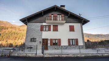 Un bâtiment à deux étages, doté d’une façade en pierre, d’un balcon et surplombant un paysage montagneux.