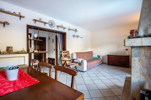 Una sala de estar con una mesa de comedor, sillas, un sofá, una chimenea y una zona de cocina con estantes.