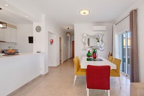 A modern kitchen with white cabinets, a fruit bowl, and a dining area with a white table and yellow chairs. - Villa 'Casa Barros' with Mountain View, Wi-Fi and Air Conditioning (Algoz)