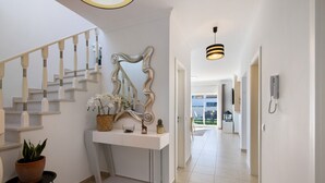 Ein modernes Interieur mit einer Treppe, einem Konsolentisch mit Dekoration und einer Pendelleuchte, mit Blick in einen weiteren Raum.