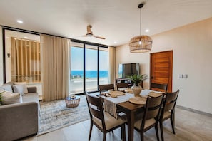 A dining area with a table set for four, a ceiling fan, and a view of the ocean through large windows.