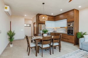 A modern kitchen with wooden cabinets, a built-in oven, and a dining area with a table and chairs.
