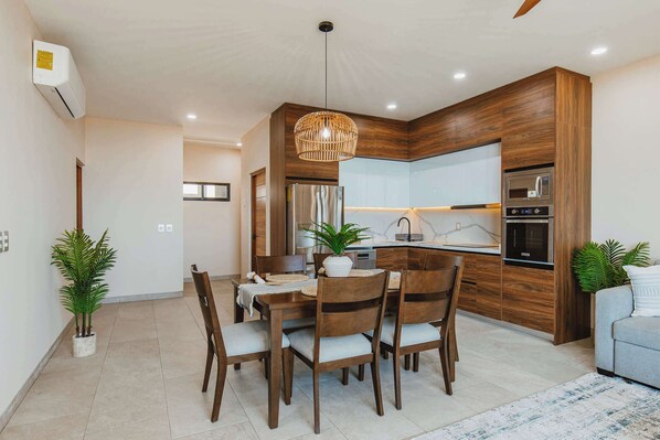 A modern kitchen with wooden cabinets, a built-in oven, and a dining area with a table and chairs.