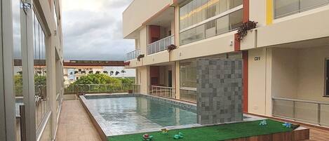 Un edificio moderno con piscina en la azotea, terraza de madera y barandillas de vidrio.