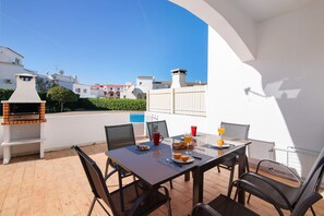 Une terrasse extérieure avec une table dressée pour le petit-déjeuner, un barbecue et une vue sur les bâtiments voisins.