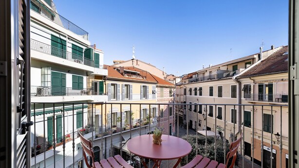 A balcony with a table and chairs, overlooking a courtyard with buildings.