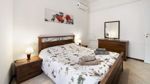 A bedroom with a bed, bedside tables, a dresser, a mirror, and an air conditioning unit.