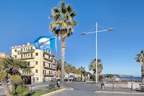 A coastal street with palm trees, a clear blue sky, and buildings with balconies.
