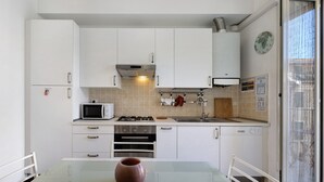 A modern kitchen with white cabinets, a microwave, stove, oven, and a glass table with a vase.