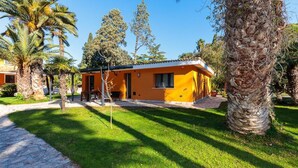 A single-story building with a flat roof, surrounded by a well-maintained lawn and palm trees. - Villa 'Dependance' with Shared Pool, Wi-Fi and Air Conditioning (Lecce)