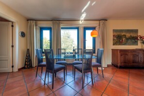 A dining area with a glass table, four chairs, a clock, and a painting on the wall.