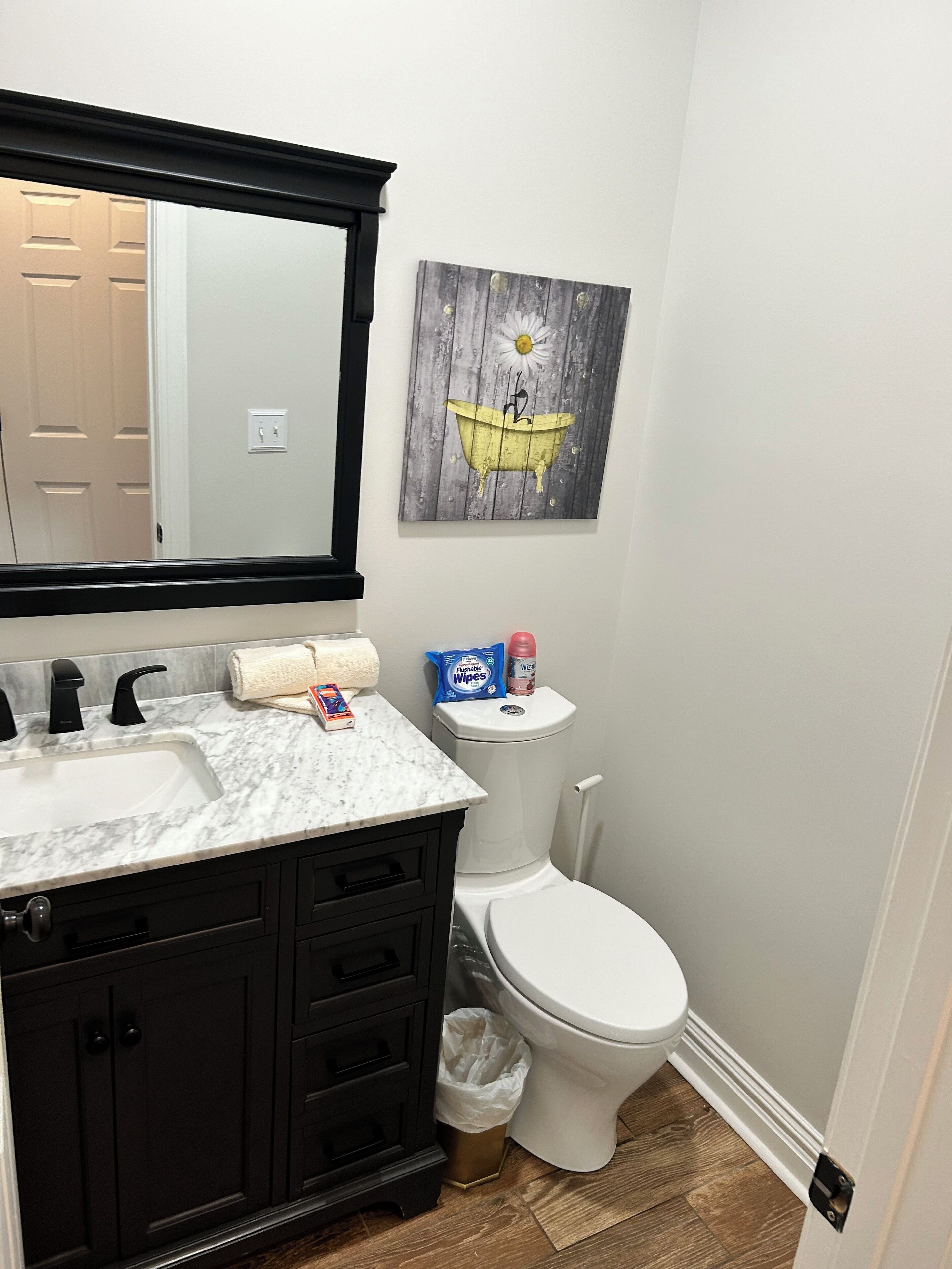 Une salle de bain avec un lavabo blanc, un meuble noir et des toilettes. On y trouve une serviette et une poubelle.