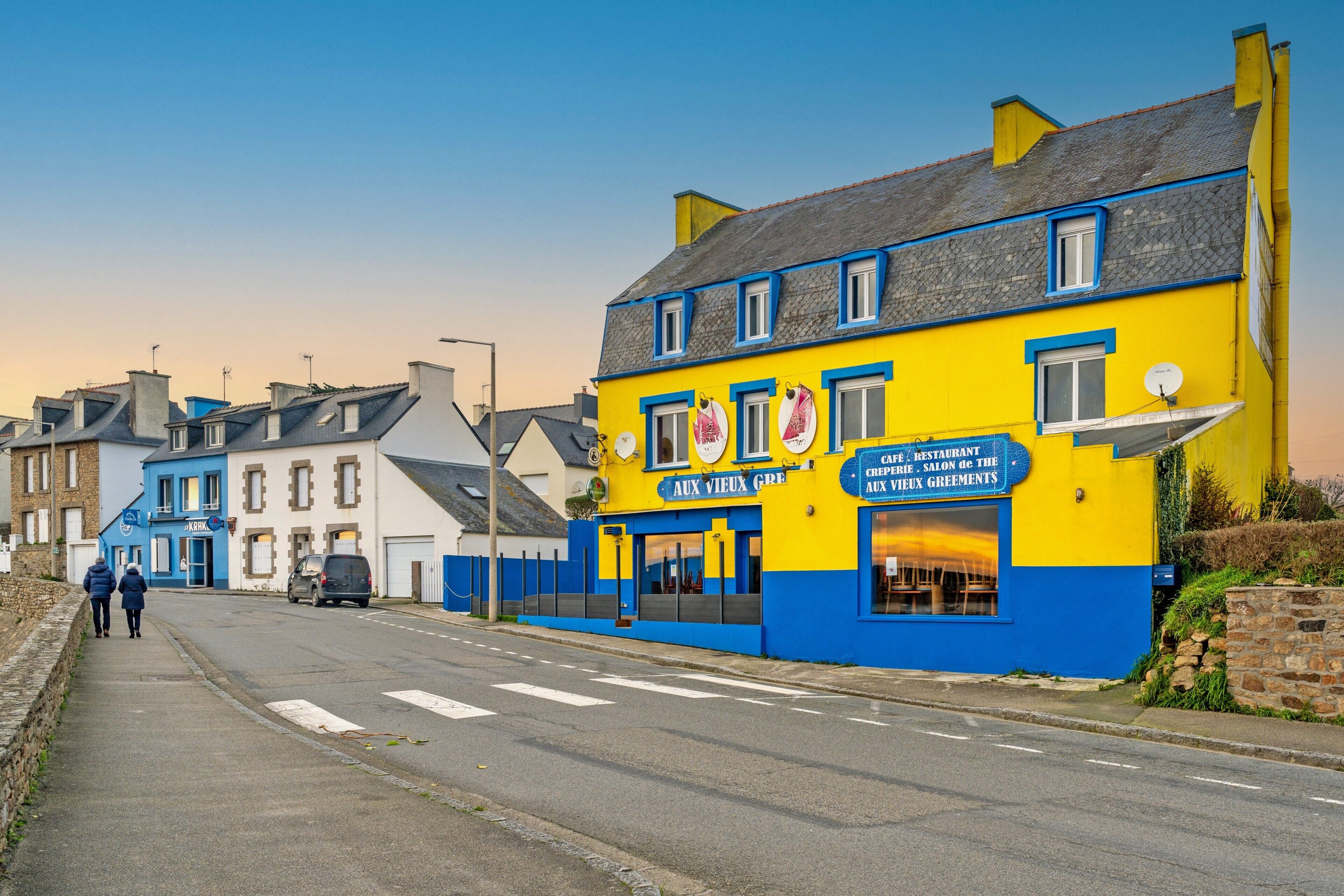 Eine Straße mit Gebäuden, darunter ein gelb-blaues Gebäude mit dem Schriftzug 'AUX VIEUX GRE'.