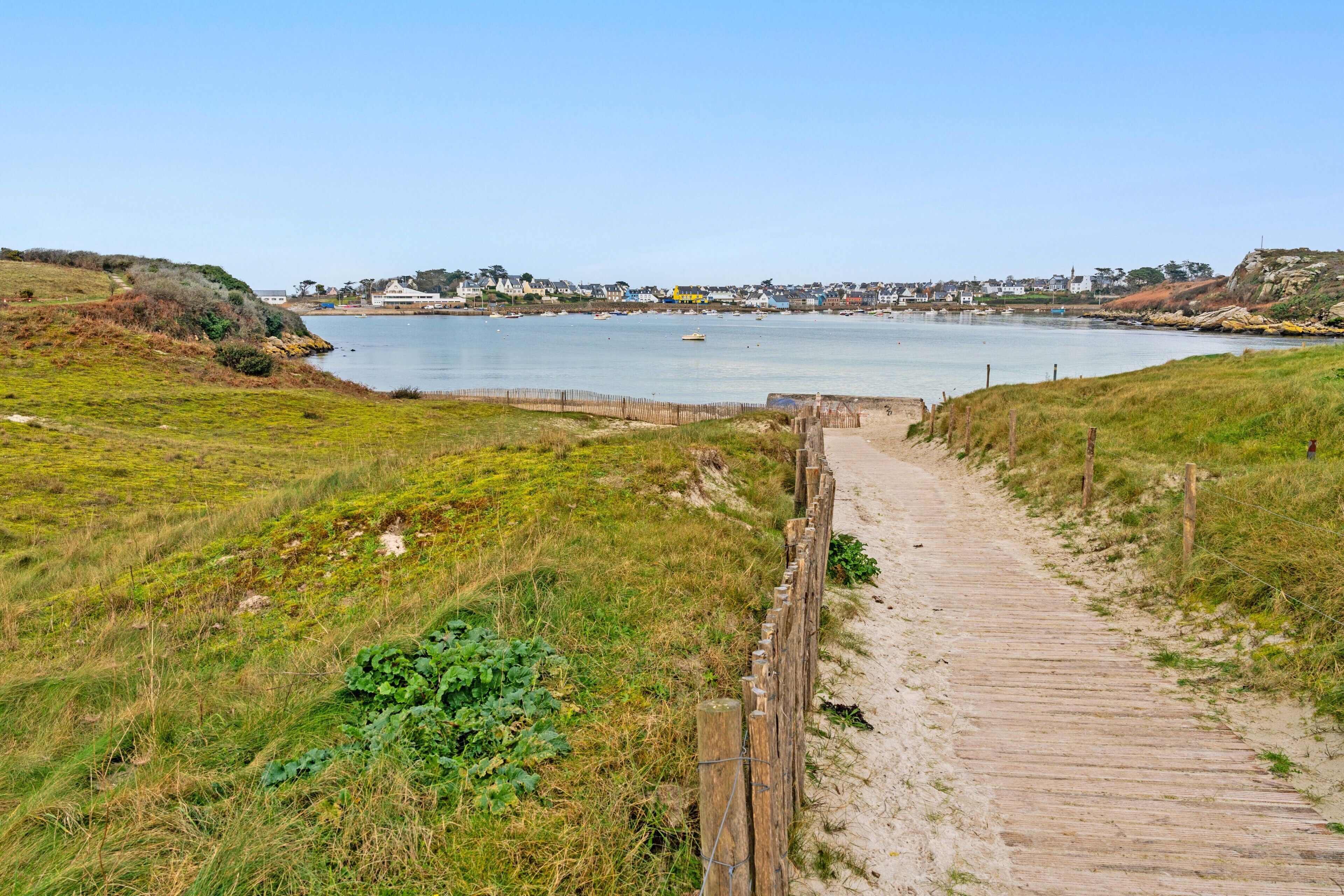 A wooden pathway leading to a body of water with a distant town.