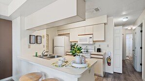 Una cocina moderna con armarios blancos, una isla central con taburetes, un microondas y una cafetera.