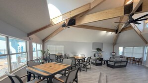 Amplia habitación tipo loft con techo alto, vigas de madera a la vista y grandes ventanales que ofrecen vistas al exterior.