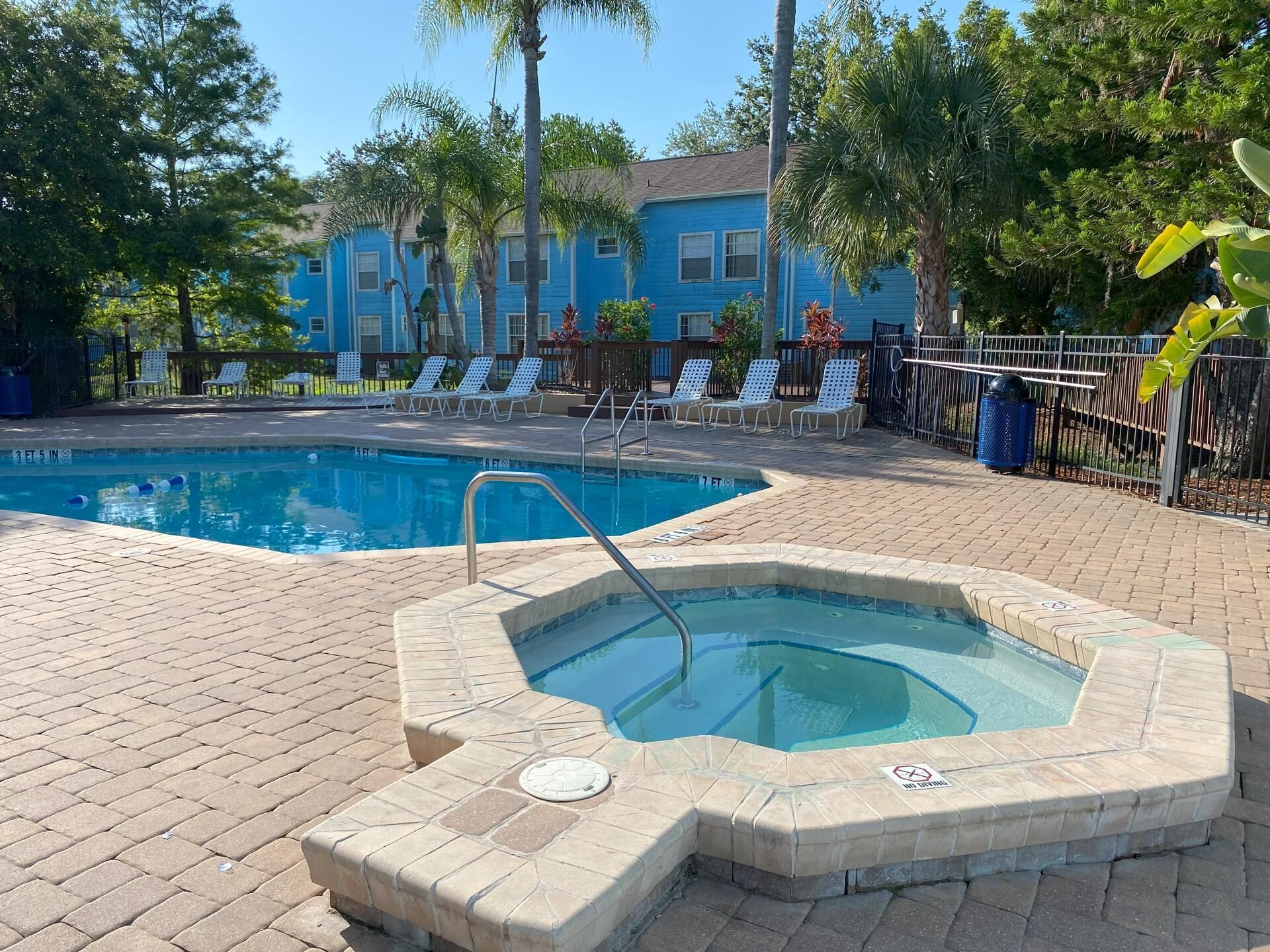 A swimming pool with a hot tub, surrounded by lounge chairs and palm trees.