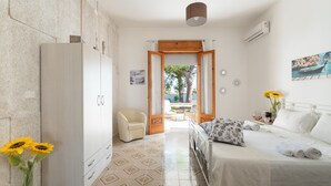 A bedroom with a bed, a chair, a wardrobe, and a view of the outside.