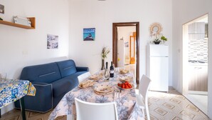 A dining area with a table set for two, a blue sofa, and a kitchen visible through an open door.