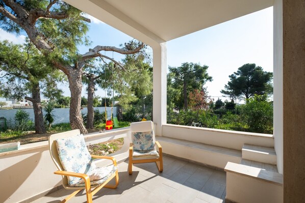 A balcony with two chairs, a view of trees and a body of water.