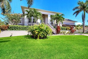 A modern house with a well-maintained lawn and palm trees. - Bikini's & Martini's Waterfront Canal: 1 Block to Beach! Dock! On Canal! Anna Maria Life (Anna Maria)