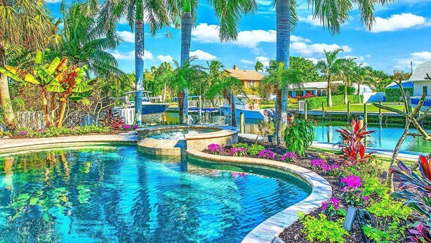 Una piscina de borde curvo, rodeada de plantas tropicales y palmeras.