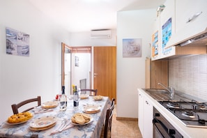 A dining area with a table set for two, a kitchen with a stove, and a door leading to another room.