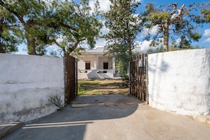 Un cancello dà accesso a un edificio con un vialetto in cemento che conduce a una casa bianca con portico.