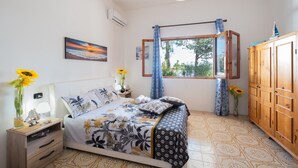 Ein Schlafzimmer mit Bett, Kleiderschrank, einem Fenster mit Vorhängen und einem Gemälde an der Wand.