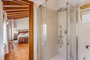 A hotel room with a glass-enclosed shower, a bed, and a wooden ceiling.