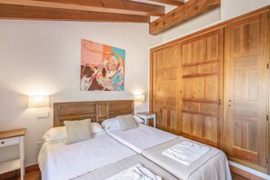 Uma cama de casal com duas almofadas, uma mesinha de cabeceira, um guarda-roupa de madeira e um quadro na parede.