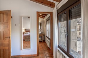 A corridor leading to a bedroom with a wooden door, a bathroom with a sink and mirror, and a window with a stone wall view. - Country House 'Fuentebuena' with Mountain View, Private Terrace and Wi-Fi (Matabuena)