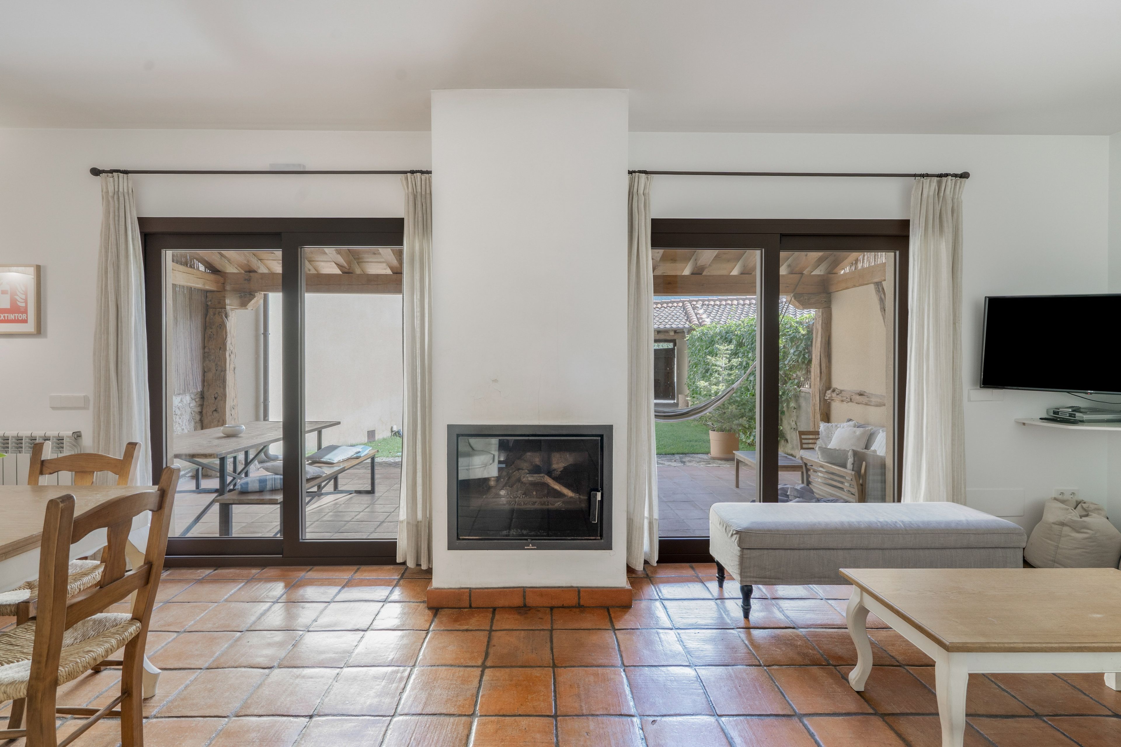 Una sala de estar con chimenea, un televisor montado en la pared y un comedor con sillas y una mesa.
