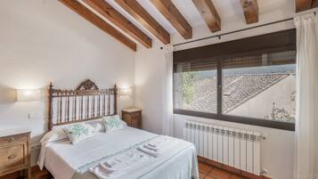 A bedroom with a bed, bedside tables, a window with a view, and a radiator.