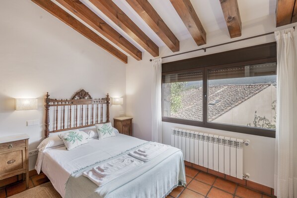 A bedroom with a bed, bedside tables, a window with a view, and a radiator.