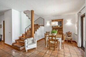 A spacious living area with a staircase, a dining table with chairs, and a kitchen area with a wooden cabinet and a hanging light fixture. - Country House 'Fuentebuena' with Mountain View, Private Terrace and Wi-Fi (Matabuena)